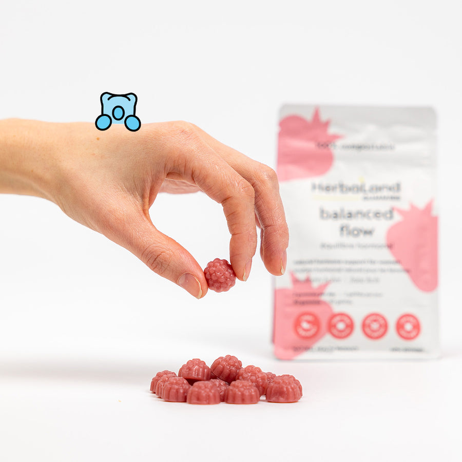 Person holding herbaland gummies, with balanced flow pouch for natural hormone support for women with lychee strawberry flavor in the background